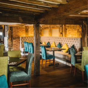 The main dining room showing blue and green high back velvet chairs and rustic wooden beams